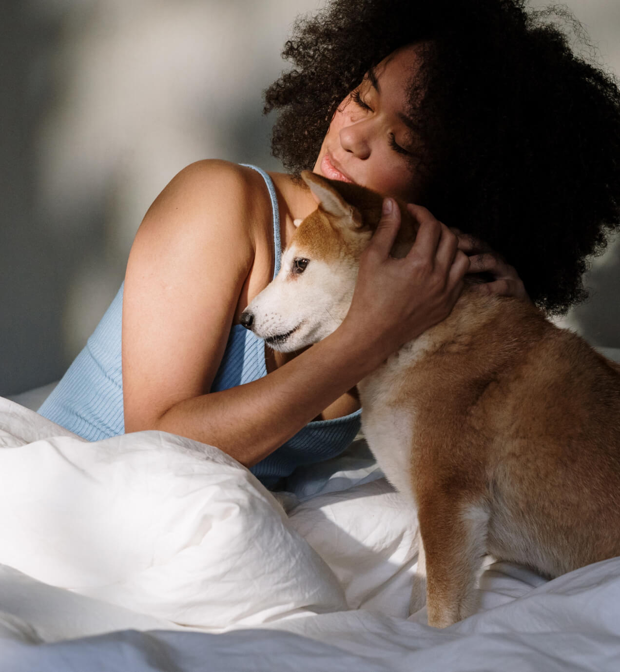 A person with dark hair and blue singlet top hugs a small dog with ginger and white fur.